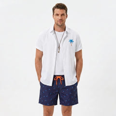 Man wearing a white palm tree print linen look cotton button up shirt and swim shorts front view on plain background