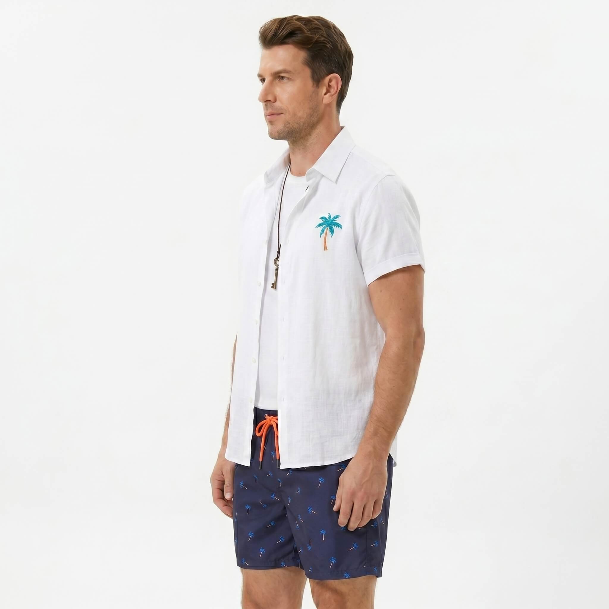 Side view of man in white palm tree print linen look shirt and swim shorts on plain background