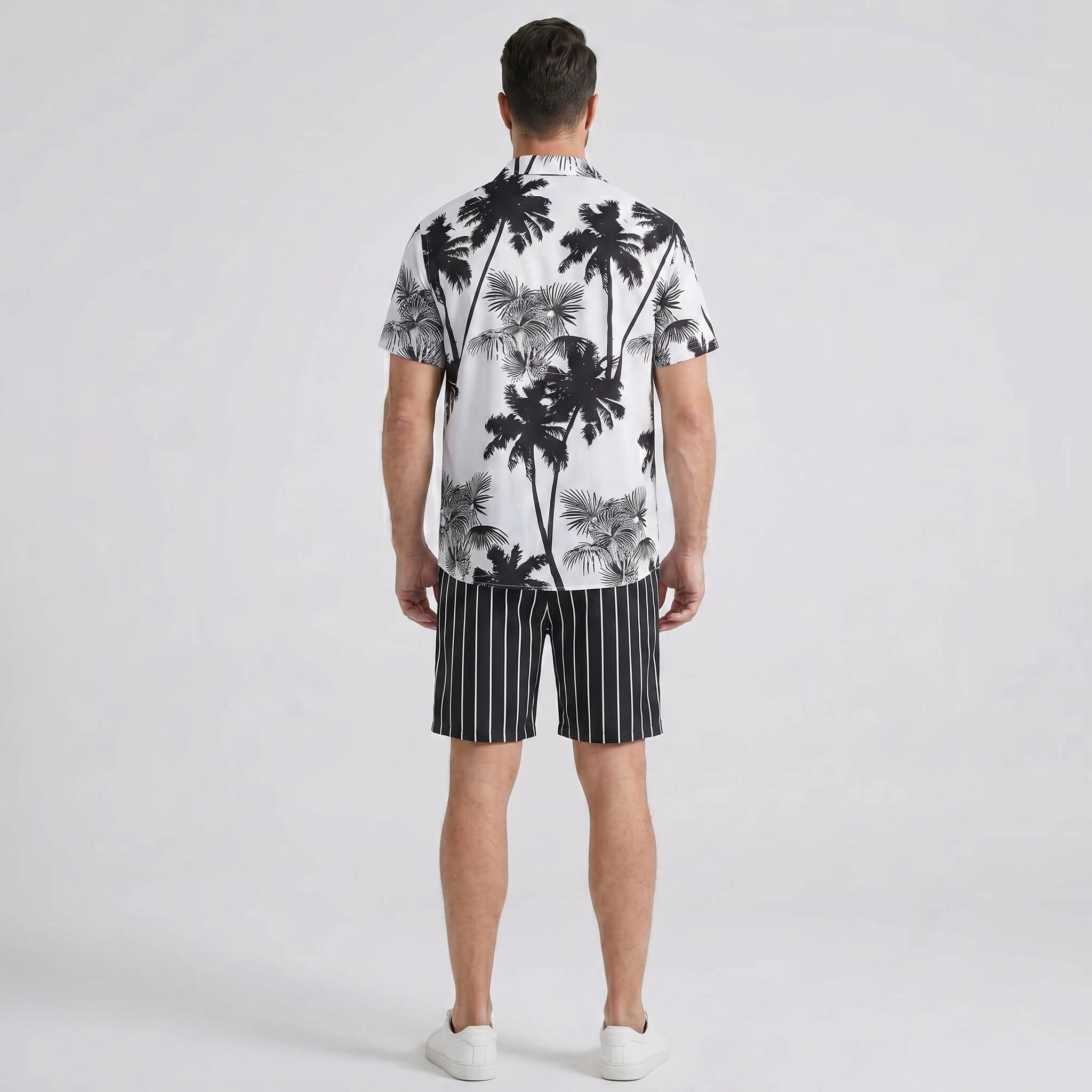 Back view of man wearing white palm trees print button up shirt and striped swim shorts