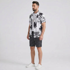 Side view of man in white palm trees print button up shirt and striped swim shorts on plain background