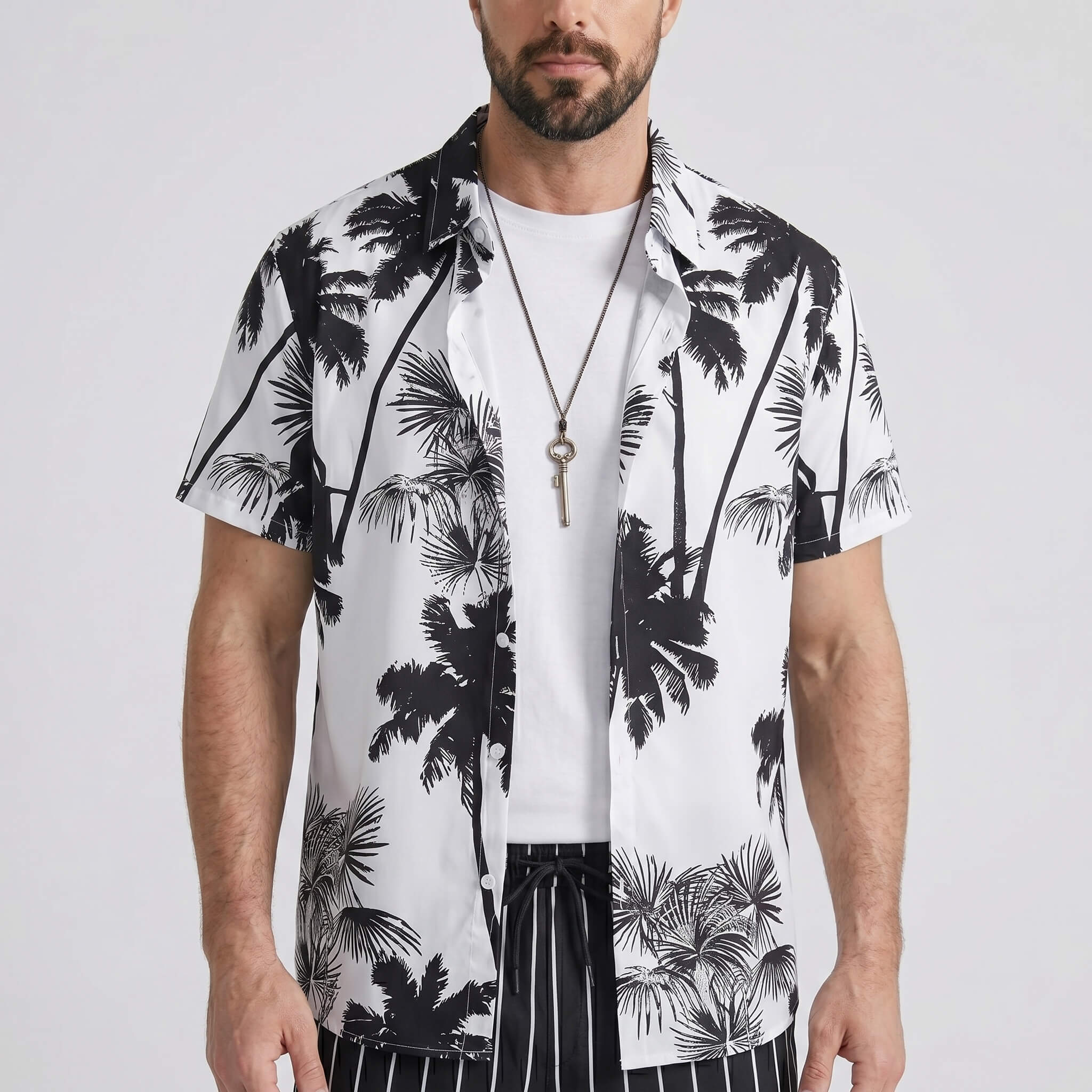 Three quarter view of man in white palm trees print shirt and striped swim shorts on plain background
