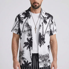 Three quarter view of man in white palm trees print shirt and striped swim shorts on plain background