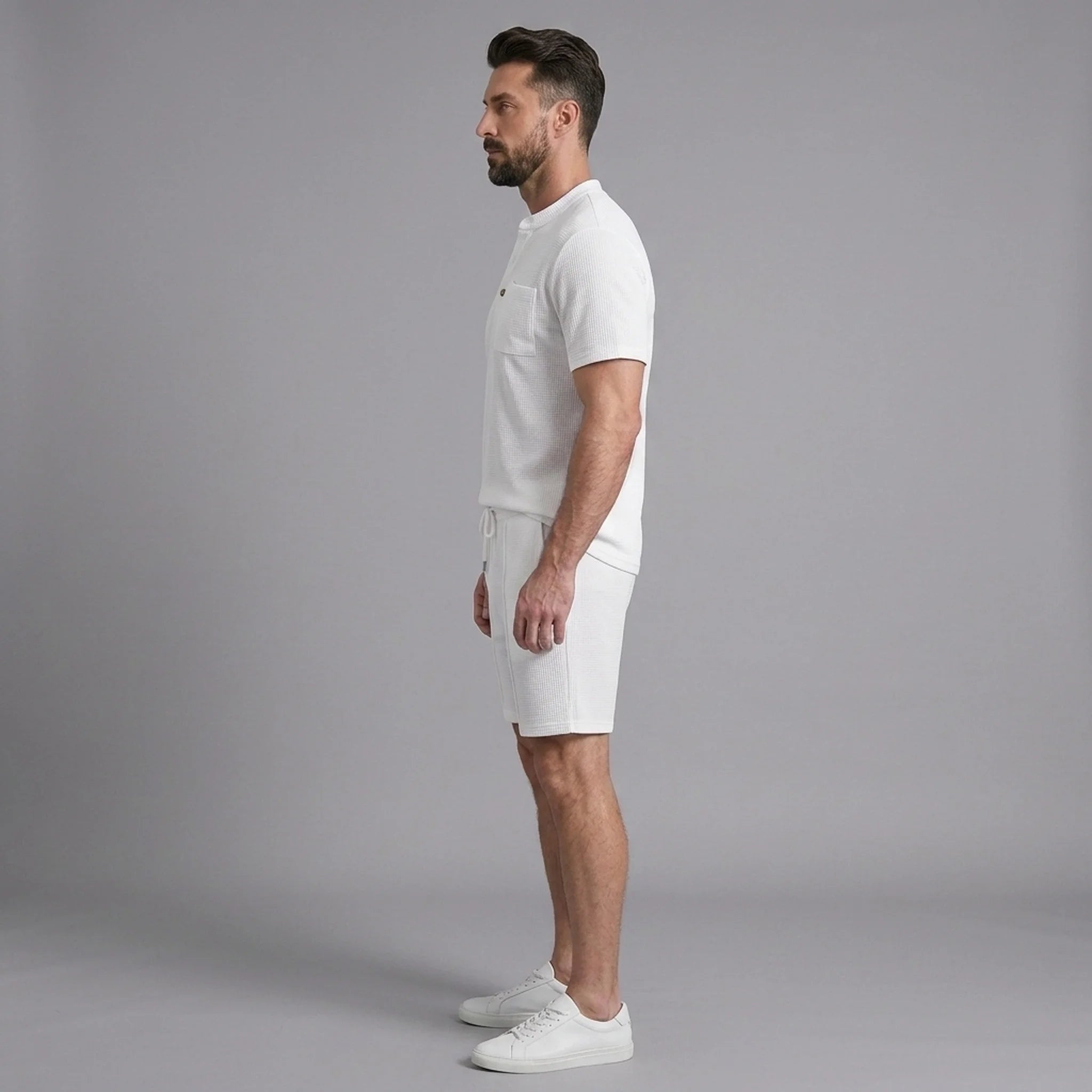 Side view of man in white waffle stand collar shirt and drawstring shorts on plain background