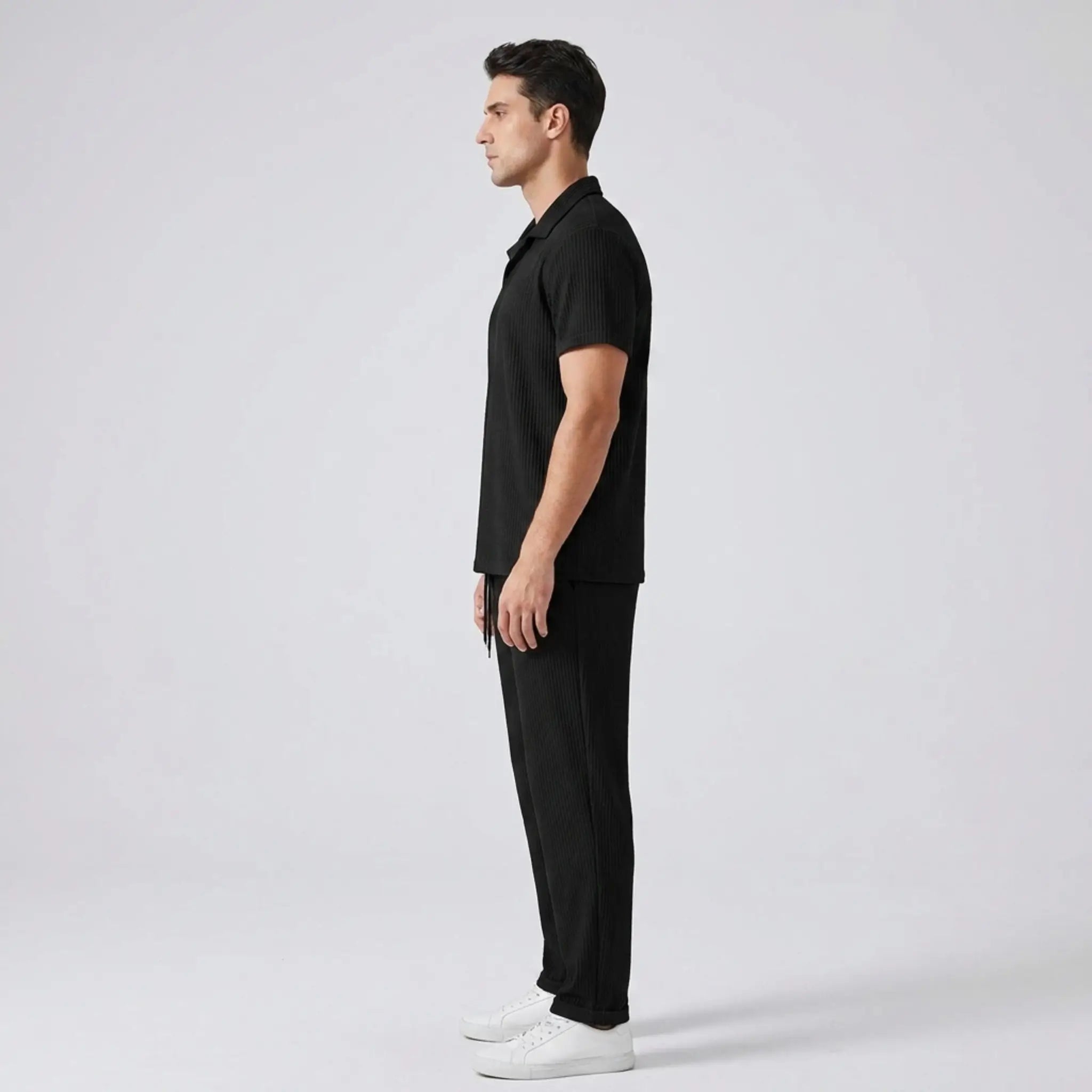 side view of man wearing a black polo shirt and trouser on a gray background